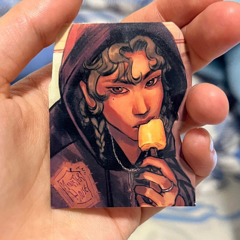 Hand holding a sticker with a stylized illustration of a character eating an popsicle