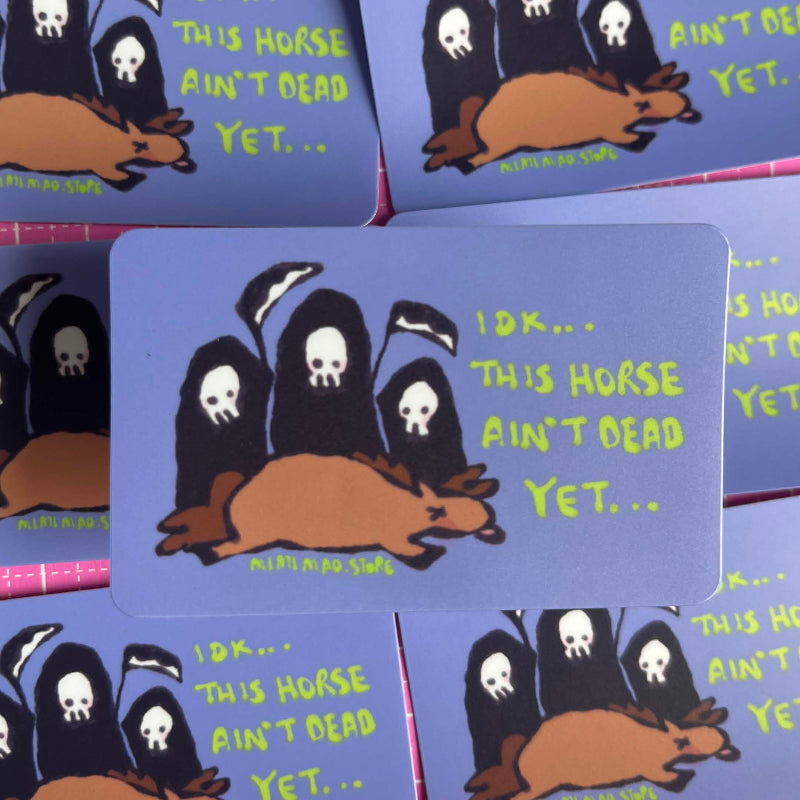 A stack of blue rectangular stickers featuring a cartoon brown horse with three black hooded figures with white skulls, and yellow text reading 'I DK.