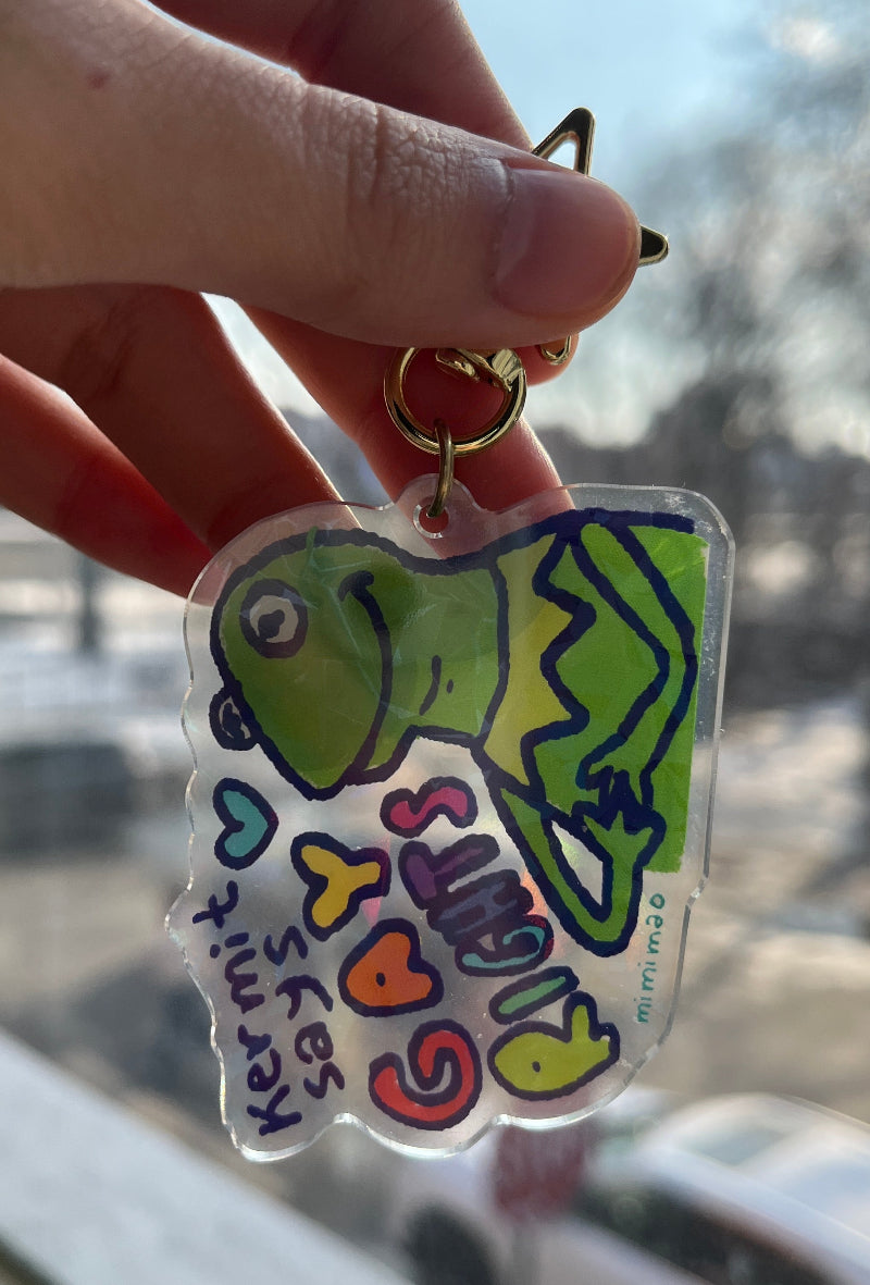 Hand holding a keychain with a colorful design of a green character and text.