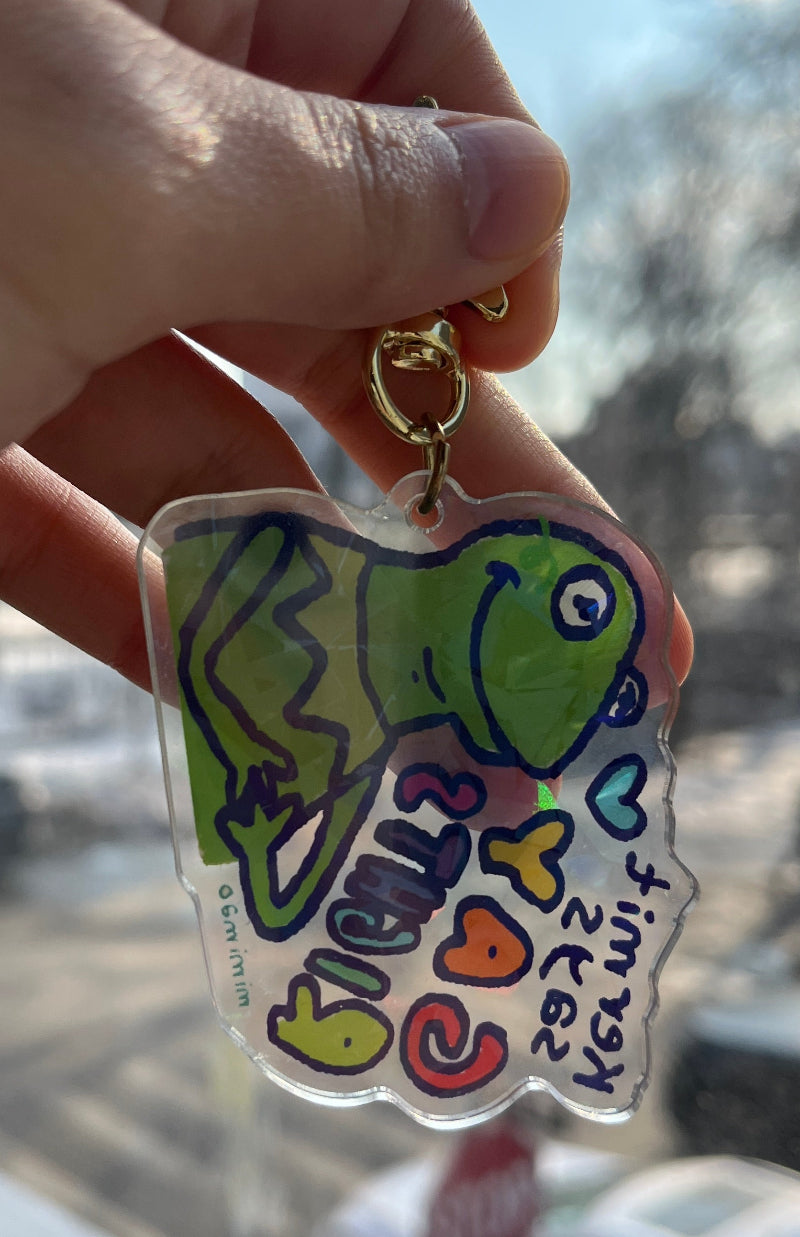 Hand holding a colorful keychain with a cartoon character and text, blurred background