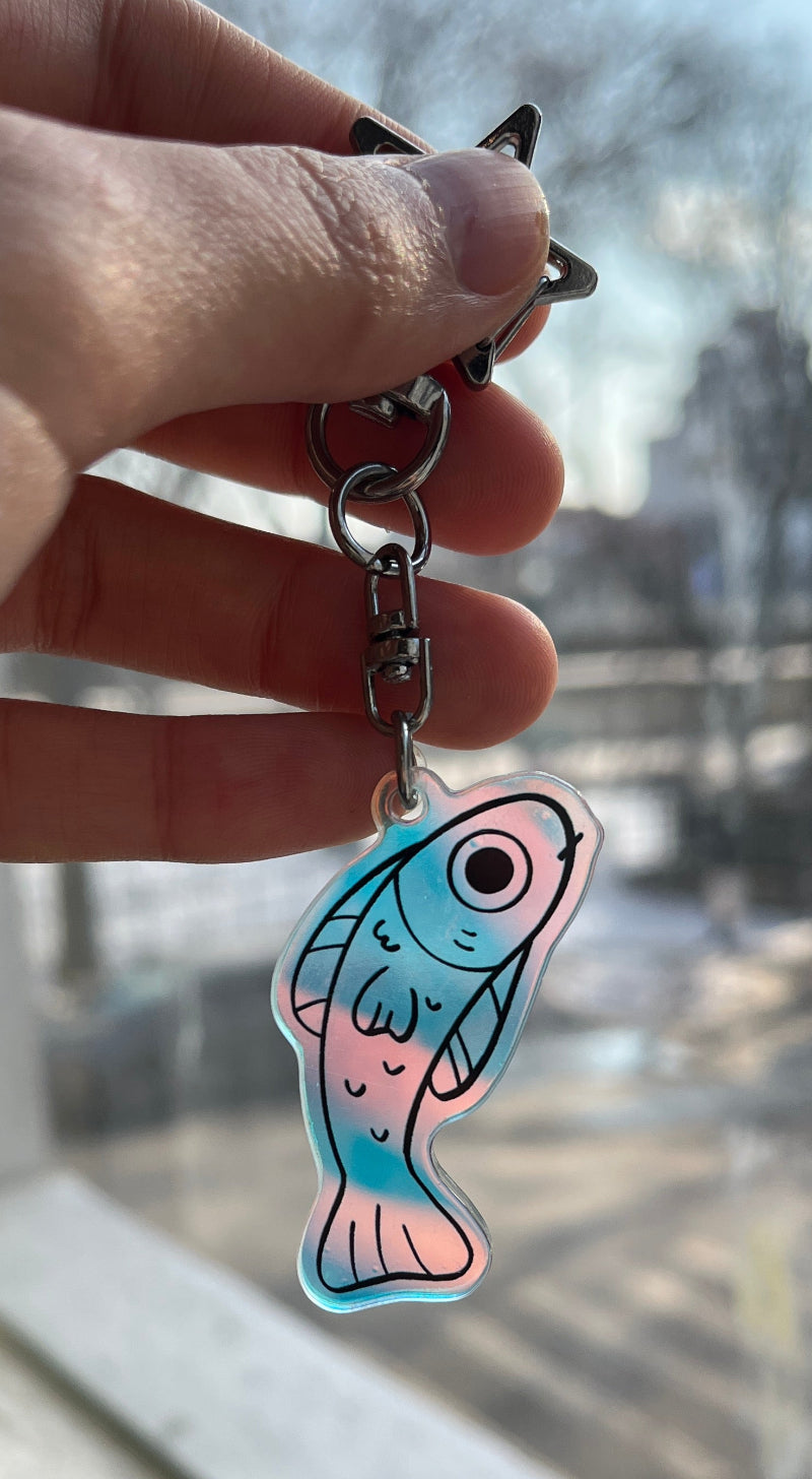 Hand holding a keychain with a fish design in front of a window