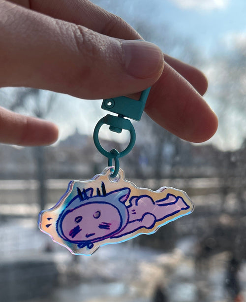 Hand holding a small colorful keychain with a character design, blurred cityscape in the background