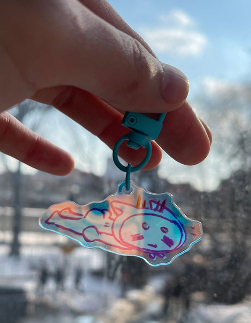 Hand holding a colorful keychain object with a cityscape in the background