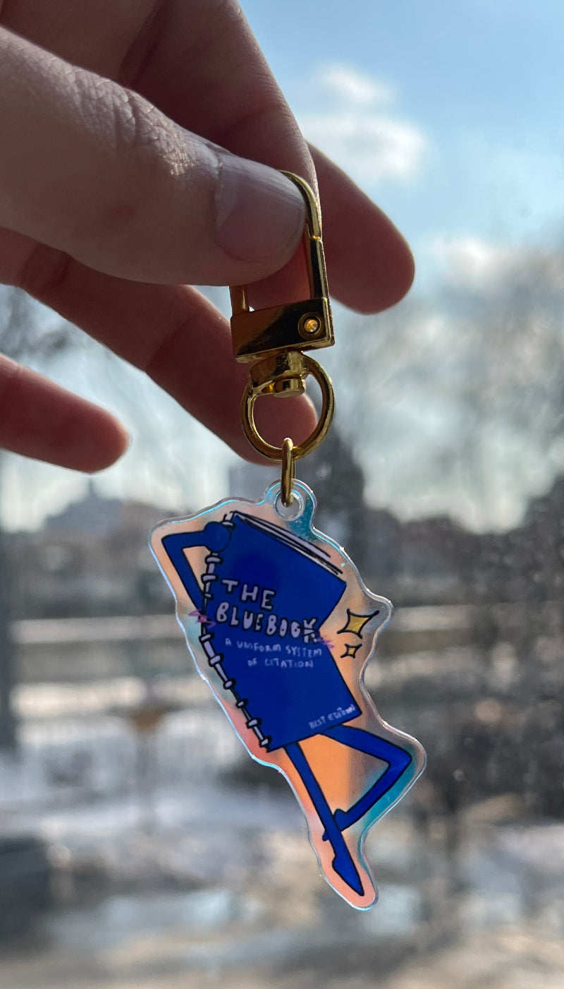 Hand holding a blue and gold keychain with a building reflection in the background
