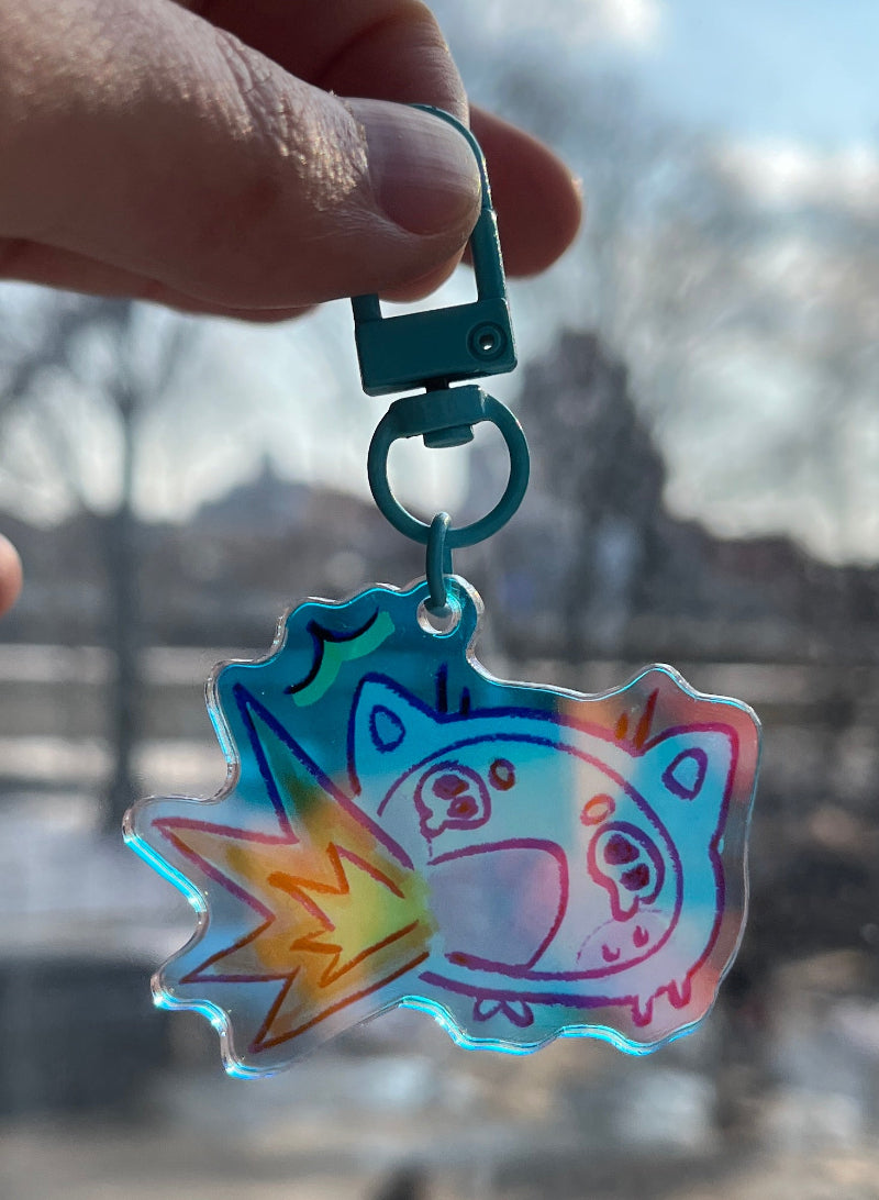 Colorful keychain with a cat design held in front of a blurred cityscape.