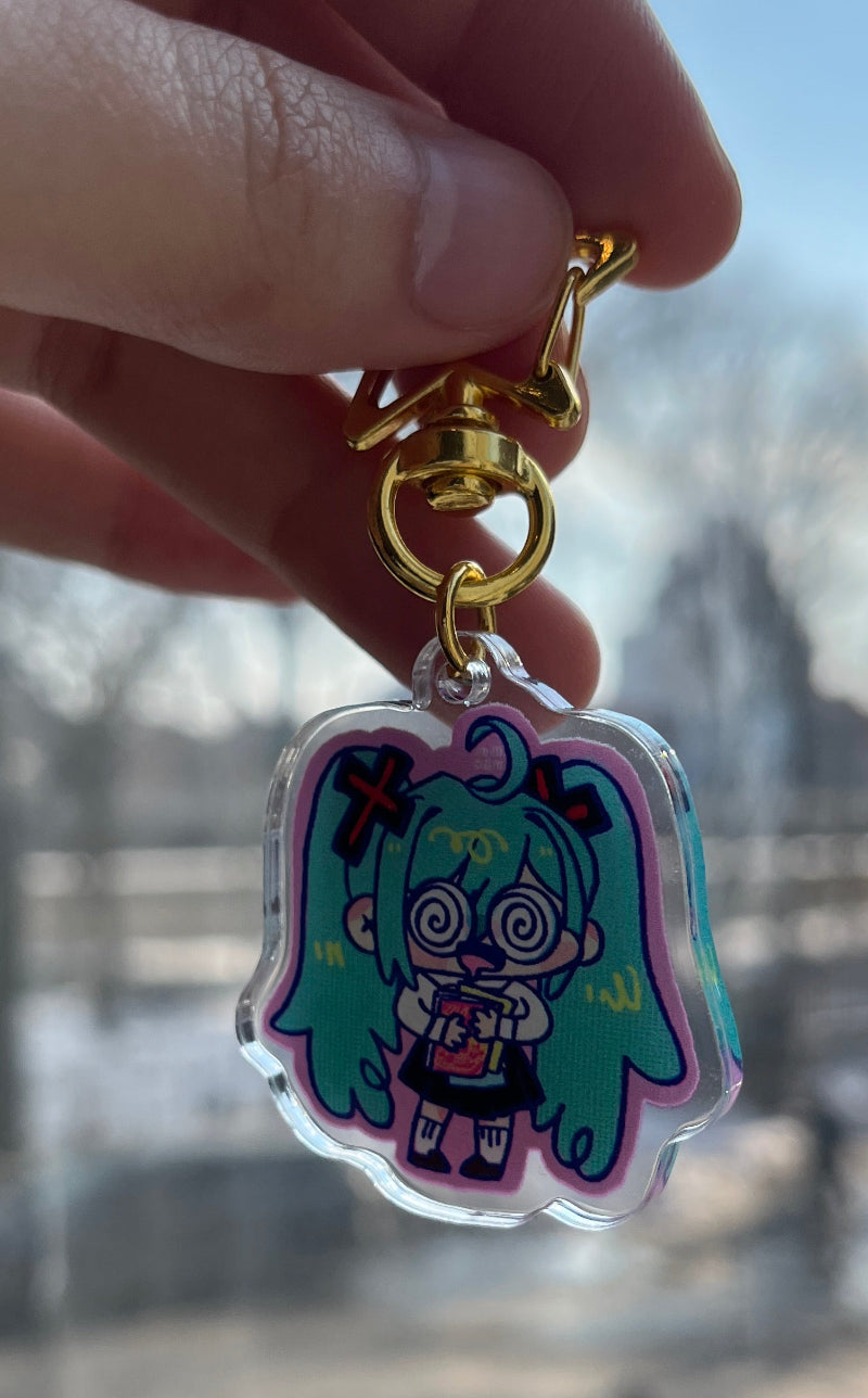 Hand holding a colorful keychain with a character design against a blurred indoor background
