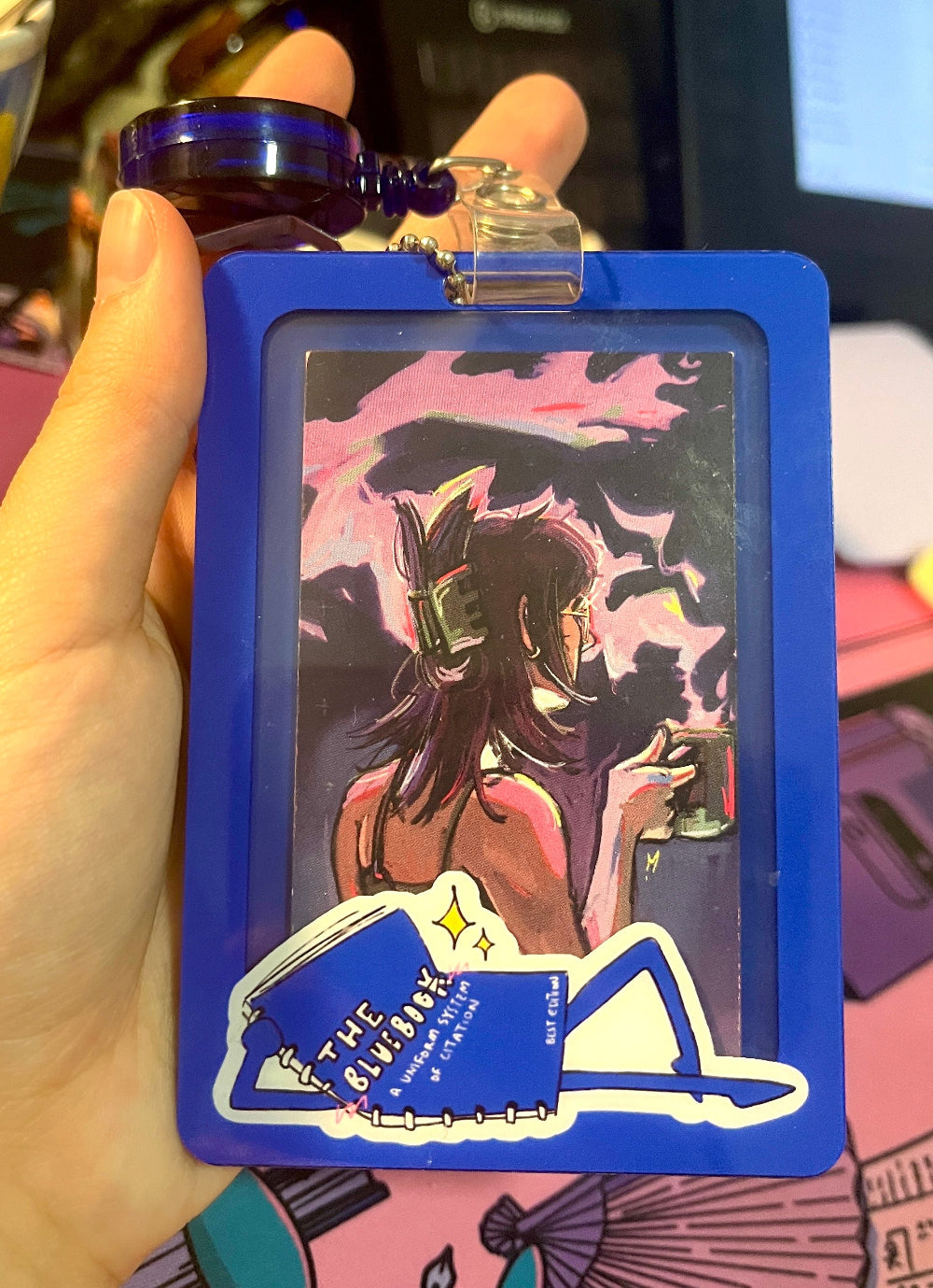 Card with artistic design of a person wearing a mask and holding a drink, framed by a blue border.