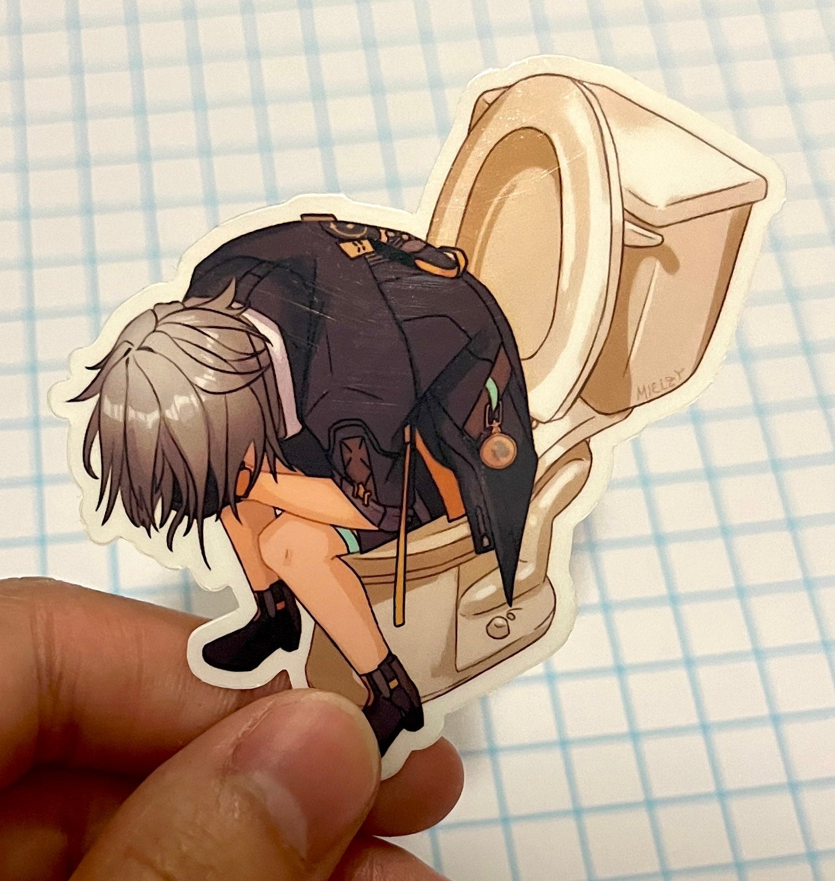 Sticker of an anime character sitting on a toilet held by a hand on a grid background