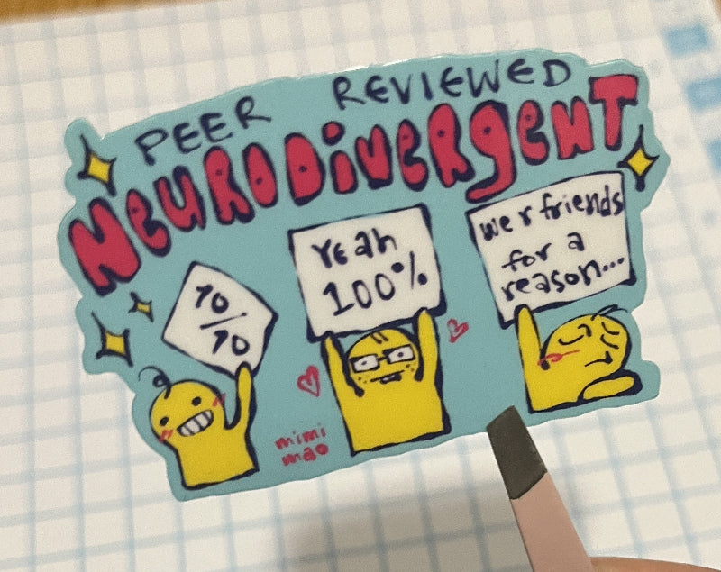 Hand holding a colorful sticker with cartoon characters on a piece of graph paper.